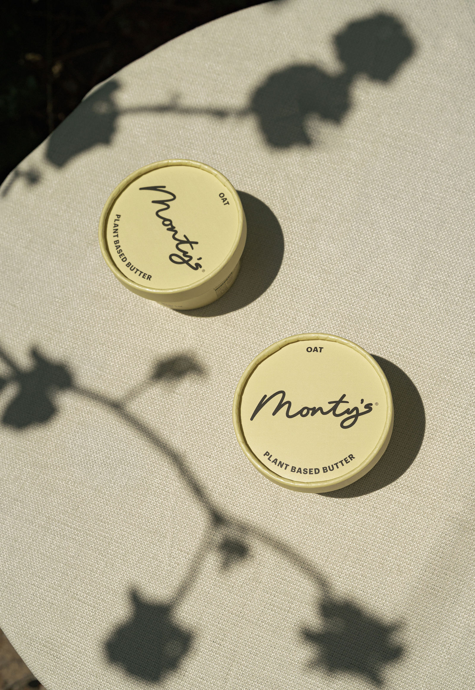 Two Monty's Oat Butter cups on a sunlit linen table with flower shadows